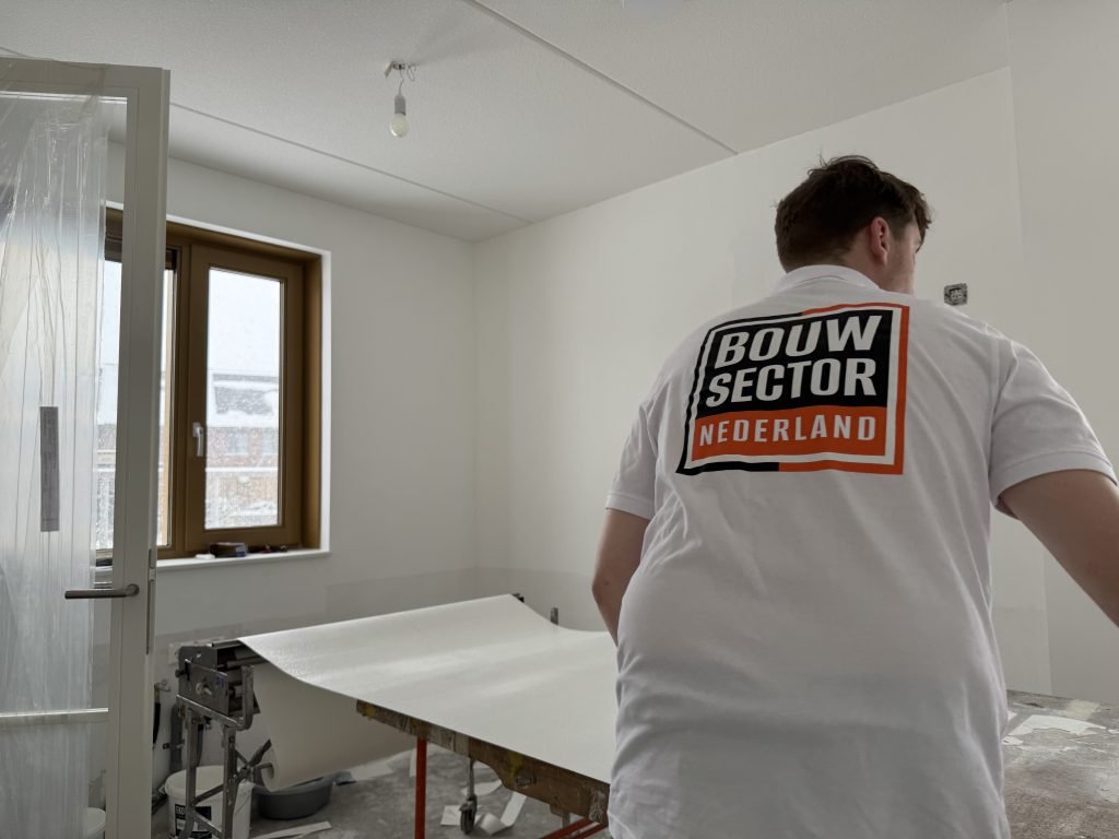 Behanger van Bouwsector Nederland rolt een baan renovlies uit over de plaktafel in een nieuwbouwkamer