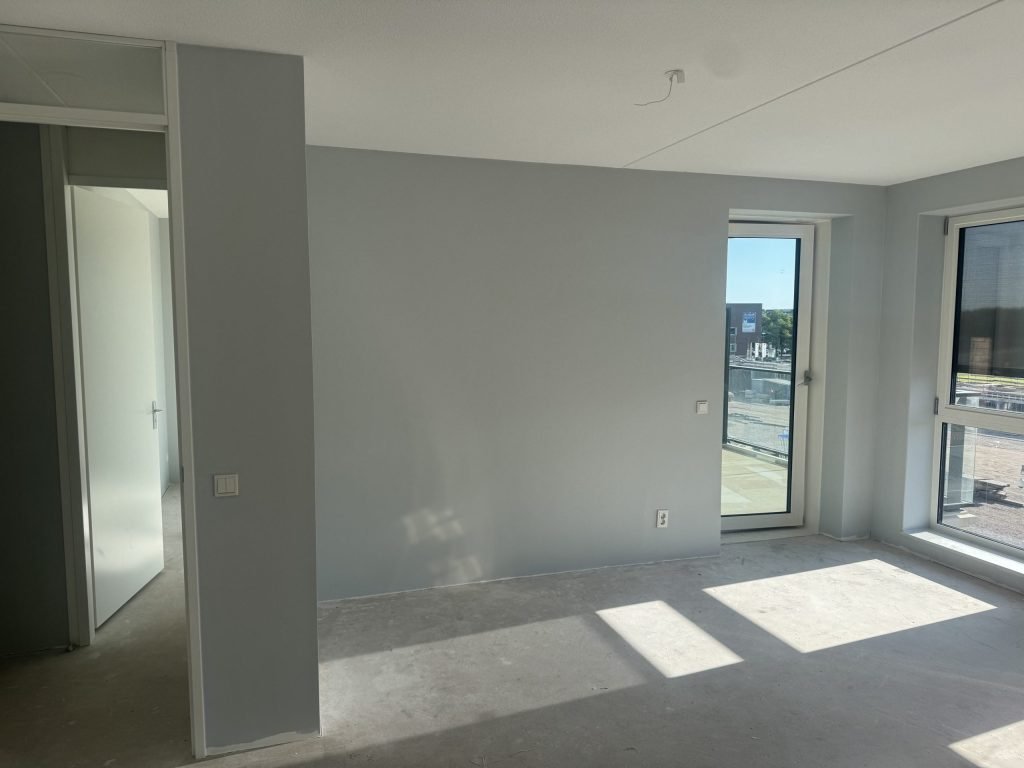 Nieuwbouwappartement met een balkondeur en lichtgrijs gesausde wanden, nog zonder vloer