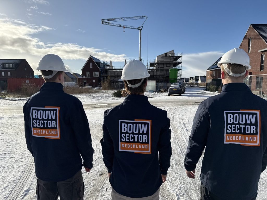 Drie vakmensen van Bouwsector Nederland met witte helm kijken naar nieuwbouwwoningen in aanbouw